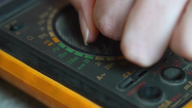 Professional electrician rotating the selector switch on a digital multimeter to measure voltage, current, and resistance for diagnosing and repairing electronic equipment in a workshop