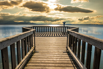 wooden pier with mountains in the distance, reflecting on calm water in the early morning light