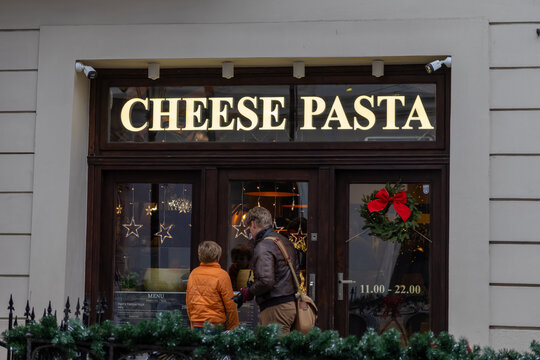 Krakow, Poland - December 2, 2025: CHEESE PASTA restaurant facade, featuring menu, hours 11.00 - 22.00, festive Christmas decor, and passersby observing