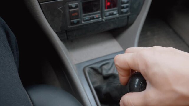 Closeup of a person's hand shifting the manual gear stick of an older car, moving through the different speeds while driving and showing the control and skill required for stick shift operation