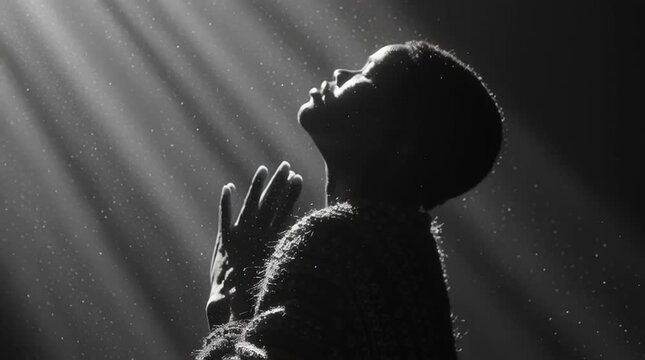 Silhouette of a person praying with hands raised in dramatic light rays. Black and white profile of spiritual worship and faith concept