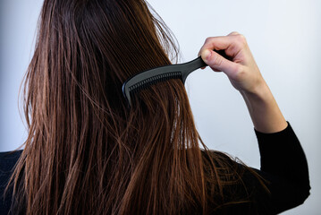 Young woman combing dirty oily hair on gray background.