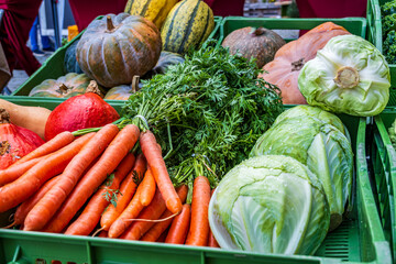 Fresh vegetables are on display at a market in the daytime, showcasing carrots, cabbage, and various types of squash
