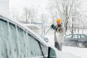 Man cleaning snow-covered car in winter