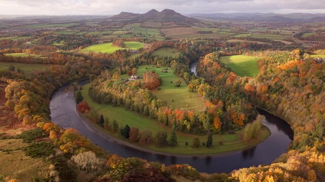 Aerial view of River Tweed snaking through the landscape, framed by autumn-tinted trees and the distant Eildon Hills, Melrose, Scotland, United Kingdom.