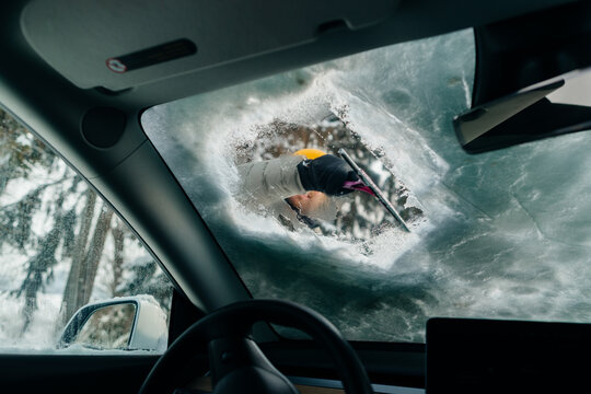 Driver clearing winter ice from car windshield