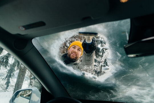 Smiling man scraping ice from car windshield in winter