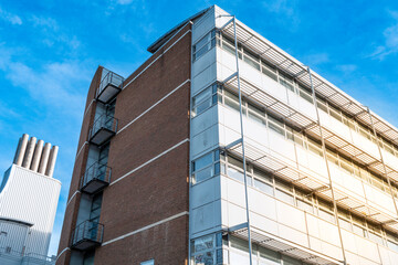 Abstract view of a famous medical research building seen in winter sunlight late in the day. A tall chimney set is in the background, located at another research centre in Cambridge, UK.