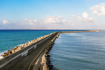 Fototapeta premium Concrete breakwater in blue sea under clear sky. Coastal landscape, maritime infrastructure, travel concept with copy space.