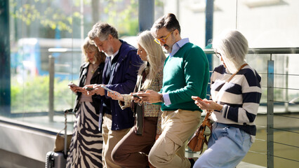 Group of diverse mature people standing in a line, focused on their phones, representing digital connectivity and waiting