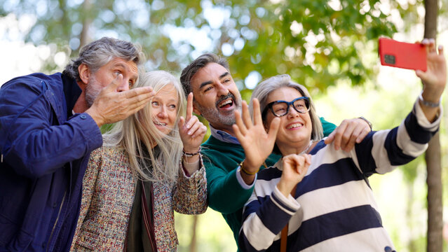 Group of happy senior friends smiling, laughing, and making expressive gestures while taking a self portrait with a smartphone outdoors