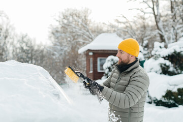 Man cleaning snow from car windshield in winter