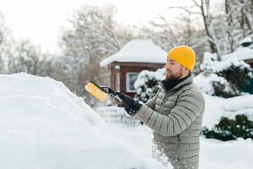 Man clearing snow from electric car windshield in winter