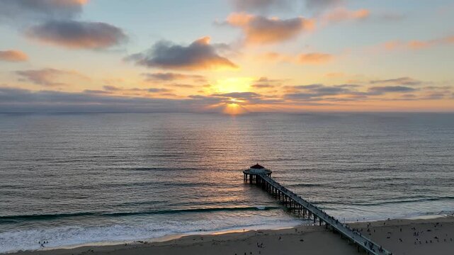 Aerial view of the pier stretching into the tranquil ocean with the sun's glow reflecting on the water's surface, Manhattan Beach, California, United States.