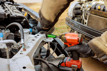 Fototapeta premium Service worker is fixing car metal frame with an electric tool while standing in an open garage during vehicle maintenance