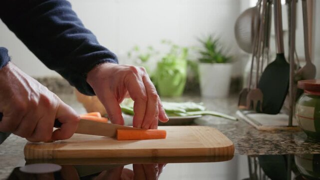 Elderly man hands cutting fresh carrot on wooden board