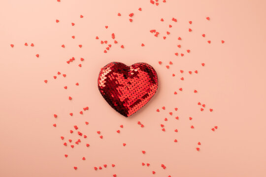 Red sequin heart on pink background with sprinkles