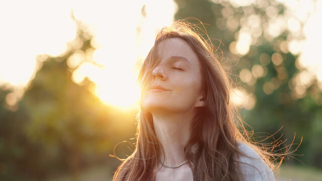 Relaxed Woman With Hair Swaying in Wind. Beautiful Woman Closing Eyes Enjoy Serene Sunset on Nature. Calm Brunette Model Posing at Golden Evening. 