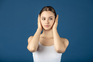 Fototapeta premium Young woman covering her ears, escaping noise or listening for silence
