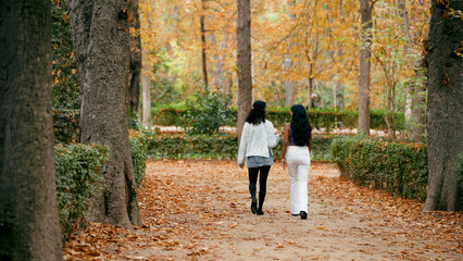 Obraz premium Two indian women strolling along a park path covered with fallen autumn leaves, enjoying friendship and conversation outdoors