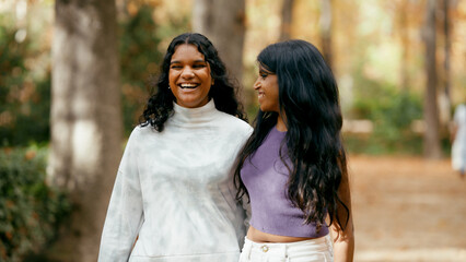Naklejka premium Two cheerful indian women enjoying a friendly conversation and laughing outdoors in a park during autumn