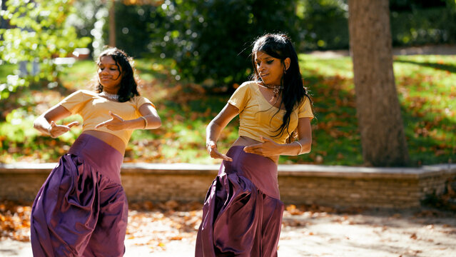 Two indian women performing traditional dance moves outdoors in a park, celebrating culture and artistic expression