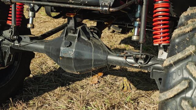 Close up on a rugged off-road utility vehicle suspension. The muddy tire, red shock spring, and axle highlight the power and adventure of extreme motorsports on a dirt track. Bright sunlight