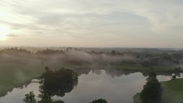 Aerial view of the lake and mist over the trees creating a scenic and serene landscape at sunrise, Ripley, England, United Kingdom.