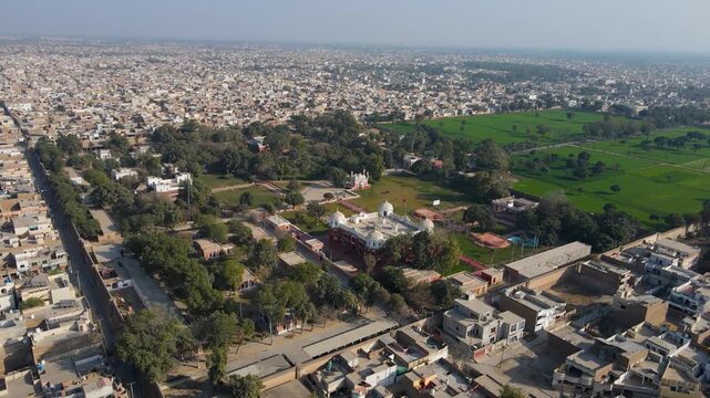 Aerial view of the white and red palatial Barbar mahal bahawalpur amidst green lawns and trees, framed by the cityscape, Bahawalpur, Punjab, Pakistan.