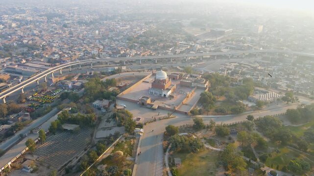 Aerial view of the Shrine of Bahauddin Zakariya, with its intricate brickwork and white dome, contrasting with the surrounding urban landscape, Multan, Punjab, Pakistan.