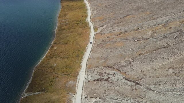 Aerial view of the contrasting blues of the lake and the browns of the landscape, separated by a narrow road in Deosai National Park, Astore, Pakistan.