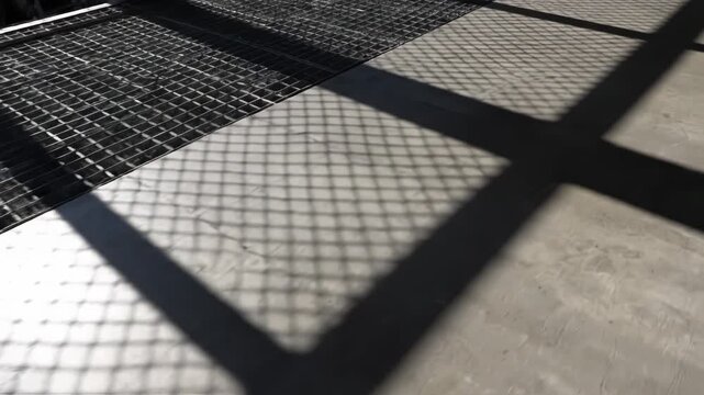Geometric shadows cast by a metal grate create a striking pattern. The interplay of light and dark forms a modern, abstract design.