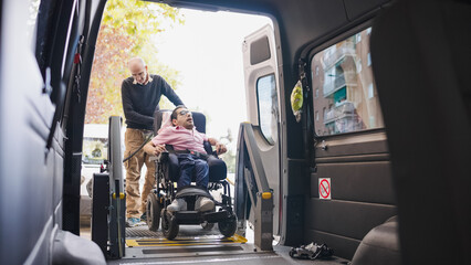 Man in wheelchair using a lift platform to enter an accessible vehicle, assisted by a caregiver, highlighting mobility and inclusion