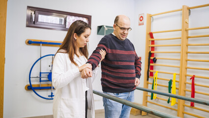Physiotherapist aiding a male patient with a long term physical condition, emphasizing assisted...