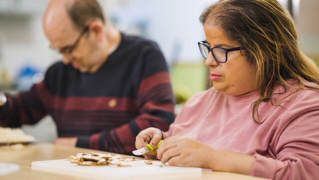 Group of adults with disabilities participating in a culinary workshop, preparing mushrooms as part of therapeutic training for independence