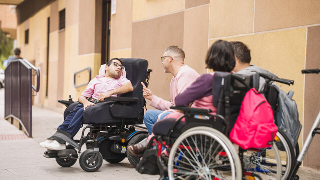 Group of adults with physical disabilities using wheelchairs and talking outdoors, advocating social inclusion and accessibility