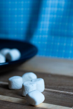 Marshmallows on wooden board with a blue background.