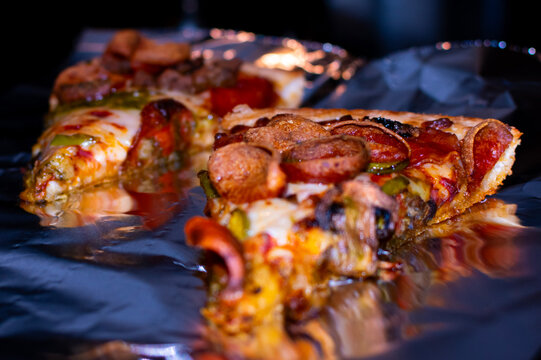 Pepperoni, peppers and mushrooms on a pizza being reheated on a sheet of foil.