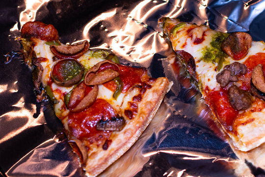 Supreme pizza with pepperoni, peppers and mushrooms being reheated on a sheet of foil.