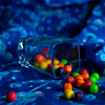 Red, green, yellow, purple and orange candies up close on a cloth blue surface. 