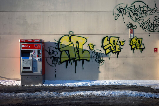 Warsaw, Masovian Voivodeship, Poland - January 20, 2026: A red and silver public transport ticket machine stands against a light-colored concrete wall covered in vibrant yellow and black graffiti tags