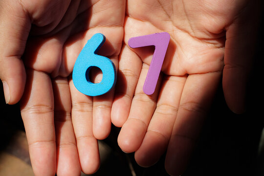 Wooden blocks showing numbers 6 and 7 held in a woman&rsquo;s hand, representing the "6-7" meme trend, playful interaction, and social media culture