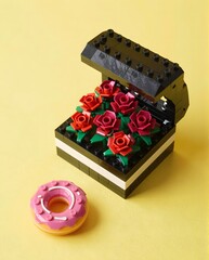 Fototapeta premium Colorful Lego Flower Arrangement in a Black Box with a Pink Iced Donut on a Yellow Background