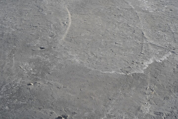 The gray backdrop of drying hand-mixed concrete. Waves of lime from river sand and the silhouettes of crushed stone edges appearing on the surface as the cement mortar dries. A beach vibe background. 