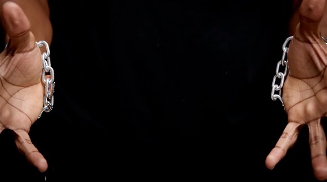 black hands forcefully breaking metal chains &mdash; symbol of freedom, liberation, and overcoming oppression, dark background