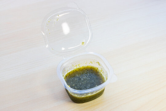 Spicy Thai seafood dipping sauce with chili, garlic, and lime in a small plastic container. Authentic zesty condiment for raw seafood, close-up view.