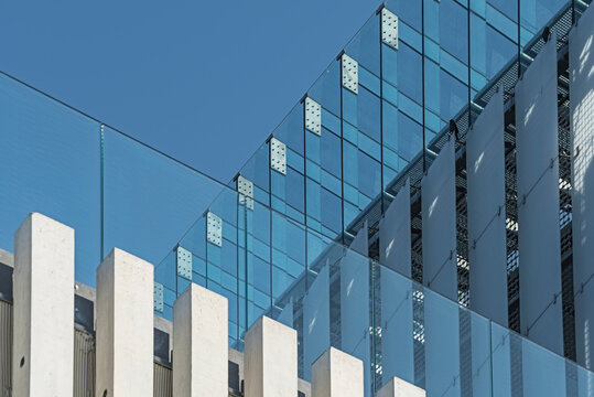 Modern glass facade with concrete columns and clear blue sky in the background.
