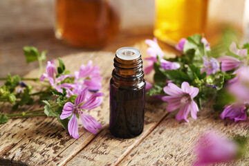A bottle of common mallow essential oil with blooming malva sylvestris twigs