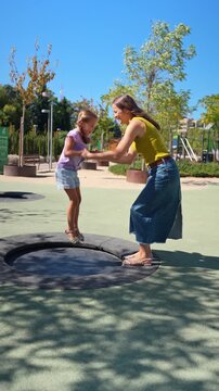 Loving mother and her happy daughter jumping on a small trampoline in a city park. Slow motion footage capturing a moment of pure joy and family fun
