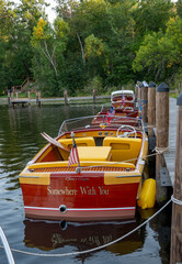 Fototapeta premium NISSWA, MN - 12 SEP 2024: Classic vintage wooden motorboat floating on the water, tied by rope to the dock on a Minnesota lake.